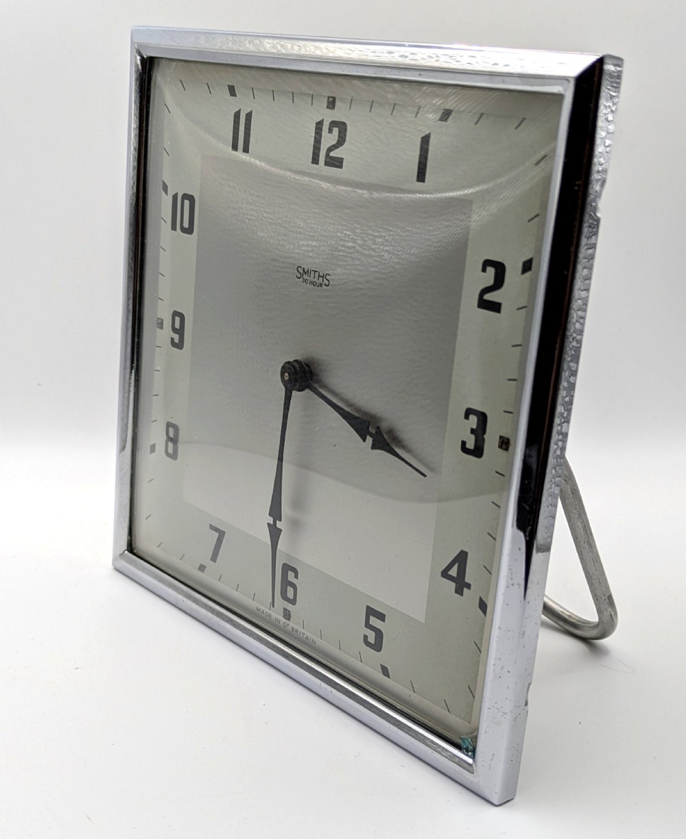 A square Art Deco chrome-framed easel clock featuring bold black Arabic numerals on a two-tone silver dial. View II