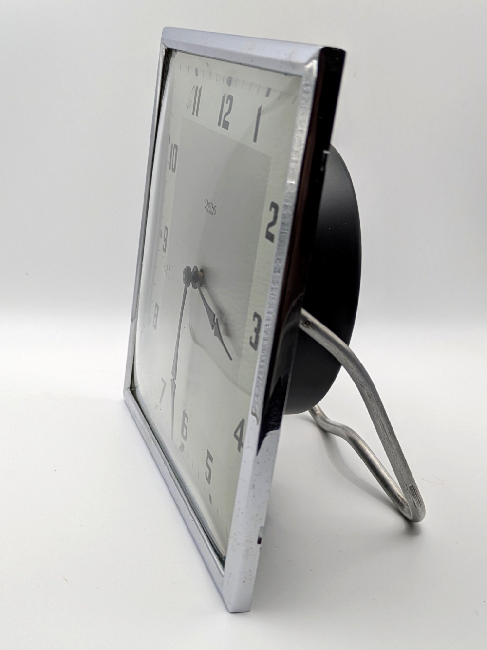 A square Art Deco chrome-framed easel clock featuring bold black Arabic numerals on a two-tone silver dial. View III