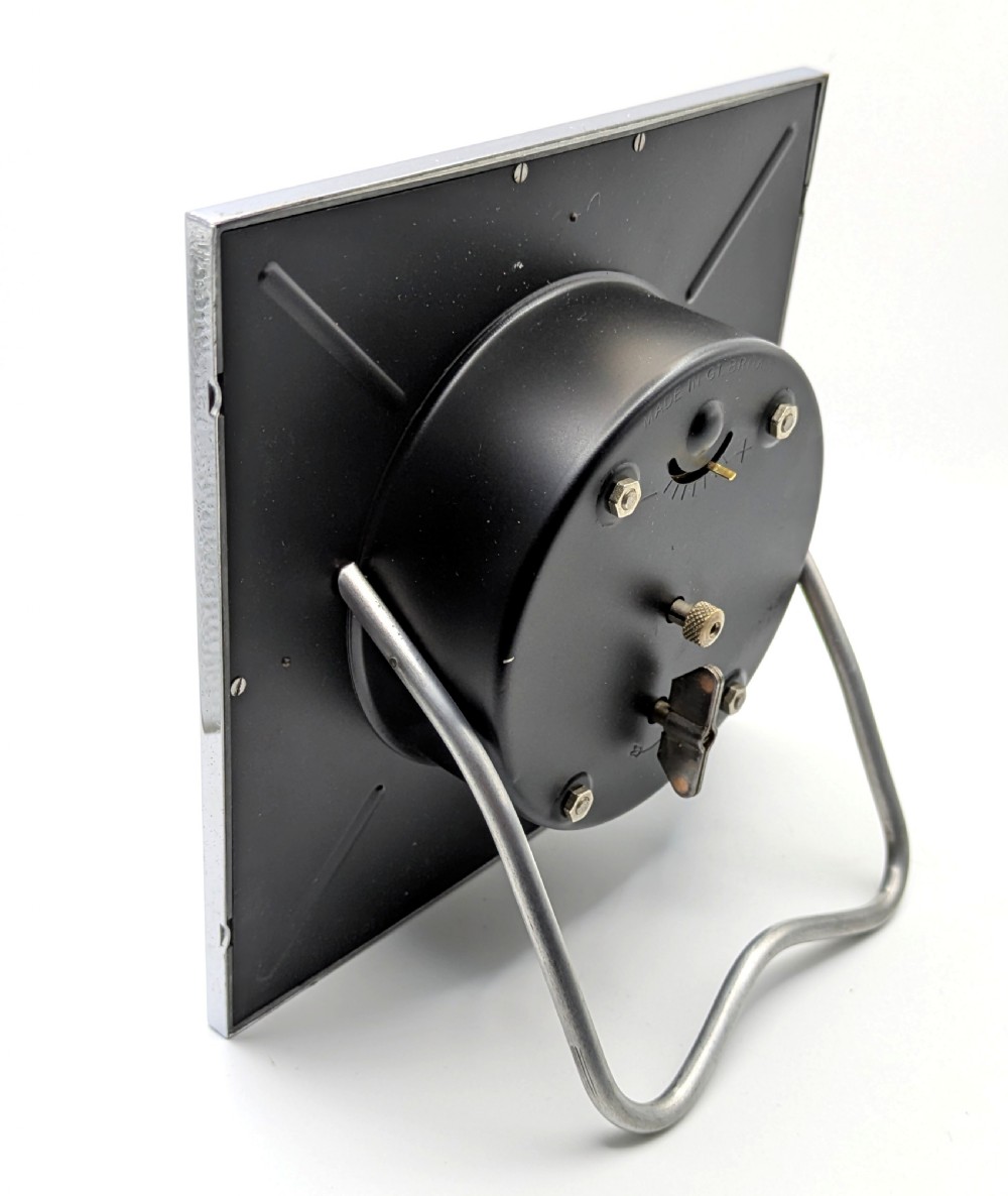 A square Art Deco chrome-framed easel clock featuring bold black Arabic numerals on a two-tone silver dial. View IV