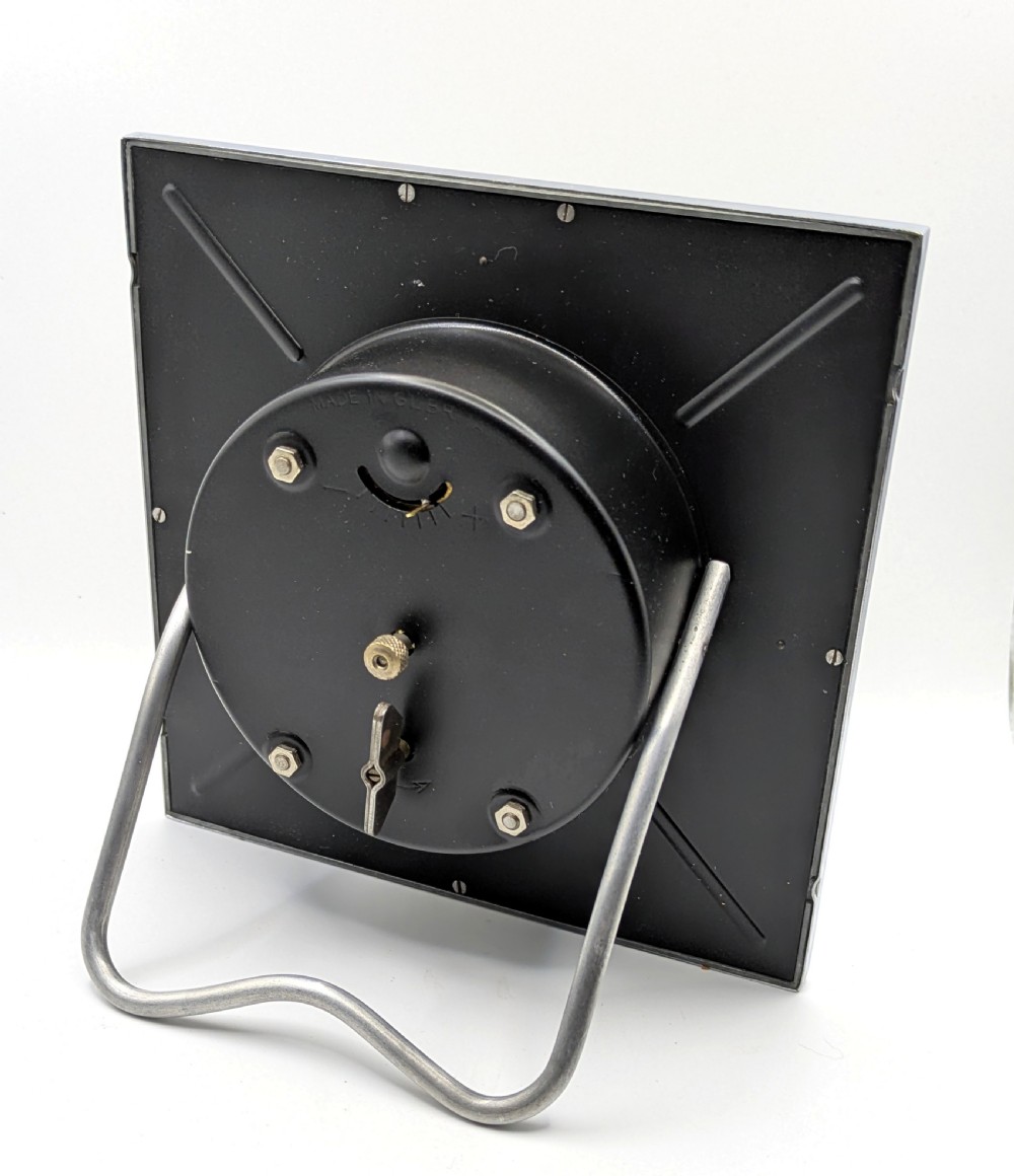 A square Art Deco chrome-framed easel clock featuring bold black Arabic numerals on a two-tone silver dial. View V