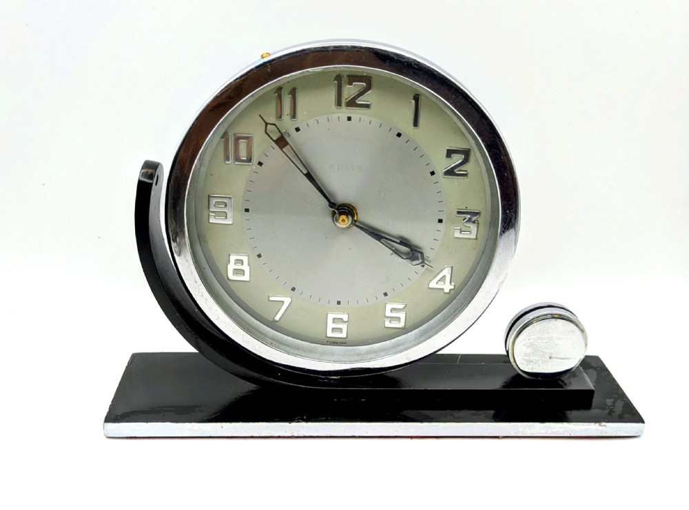 An Art Deco circular desk clock with a chrome bezel and silver dial mounted on an asymmetrical black rectangular base.