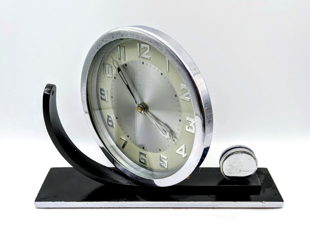 An Art Deco circular desk clock with a chrome bezel and silver dial mounted on an asymmetrical black rectangular base. View II