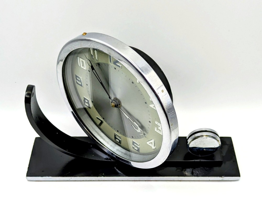 An Art Deco circular desk clock with a chrome bezel and silver dial mounted on an asymmetrical black rectangular base. View III