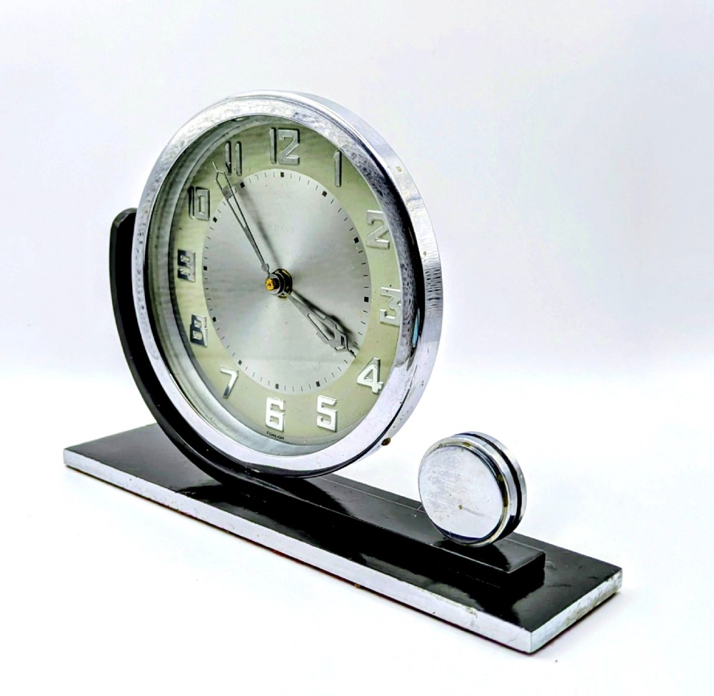 An Art Deco circular desk clock with a chrome bezel and silver dial mounted on an asymmetrical black rectangular base. View IV