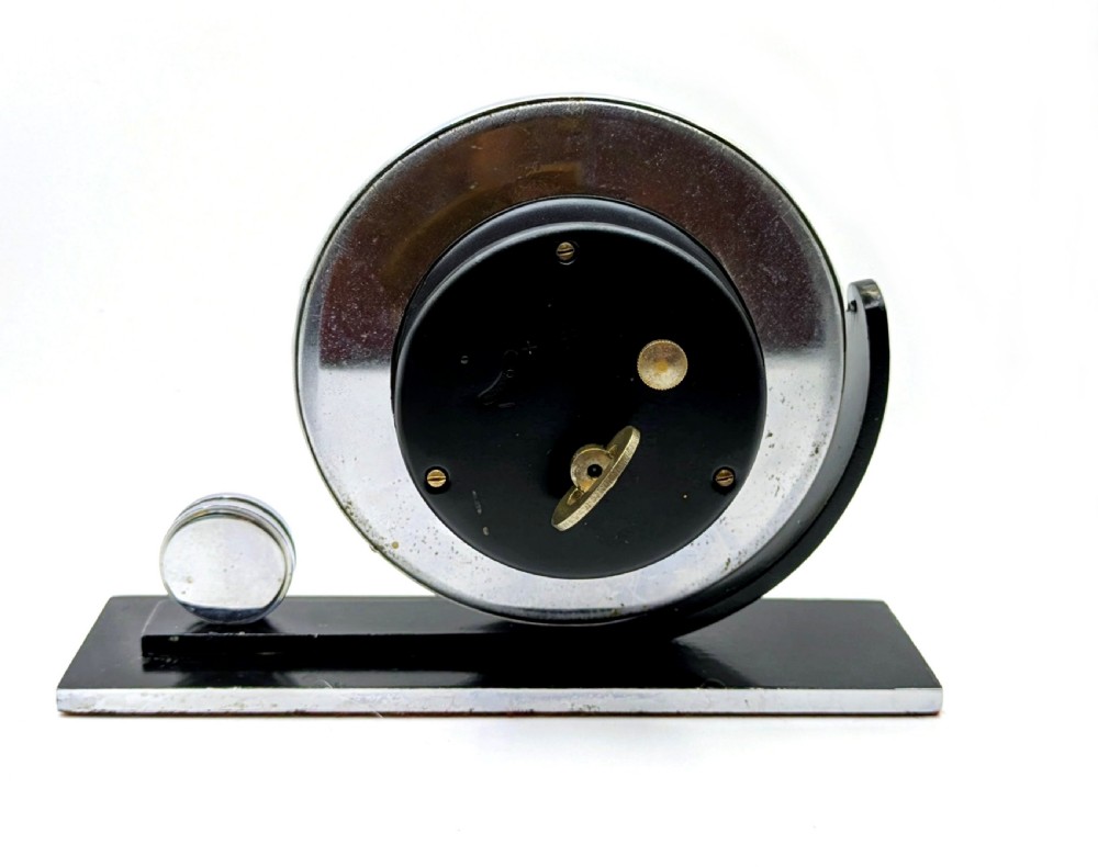 An Art Deco circular desk clock with a chrome bezel and silver dial mounted on an asymmetrical black rectangular base. View VIII