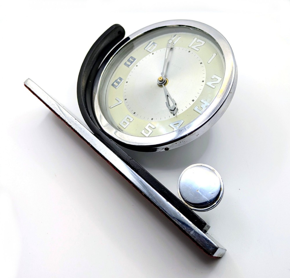 An Art Deco circular desk clock with a chrome bezel and silver dial mounted on an asymmetrical black rectangular base. View IX