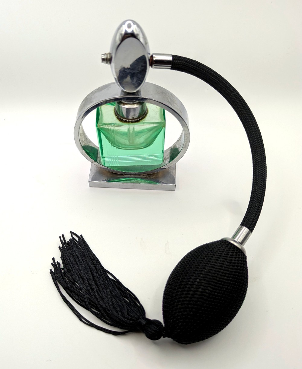 An Art Deco perfume atomiser featuring a square green glass bottle suspended inside a circular chrome frame on a rectangular base, connected to a black woven squeeze bulb with a tassel. View II