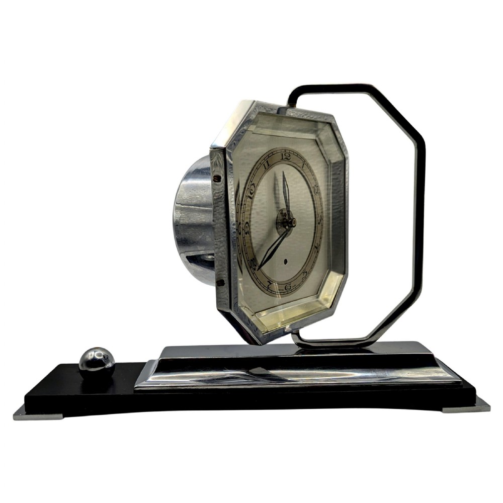 An Art Deco desk clock featuring an octagonal chrome frame mounted on a stepped base with an ebonised plinth and a small chrome sphere detail. View II