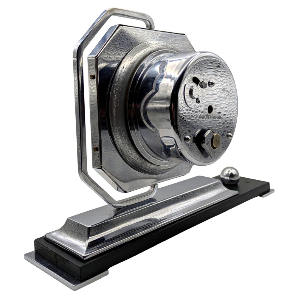 An Art Deco desk clock featuring an octagonal chrome frame mounted on a stepped base with an ebonised plinth and a small chrome sphere detail. View VII