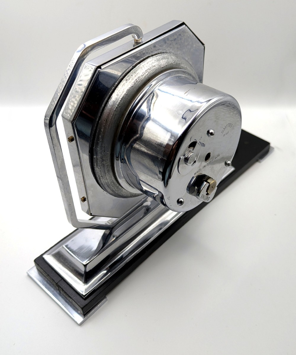 An Art Deco desk clock featuring an octagonal chrome frame mounted on a stepped base with an ebonised plinth and a small chrome sphere detail. View VIII