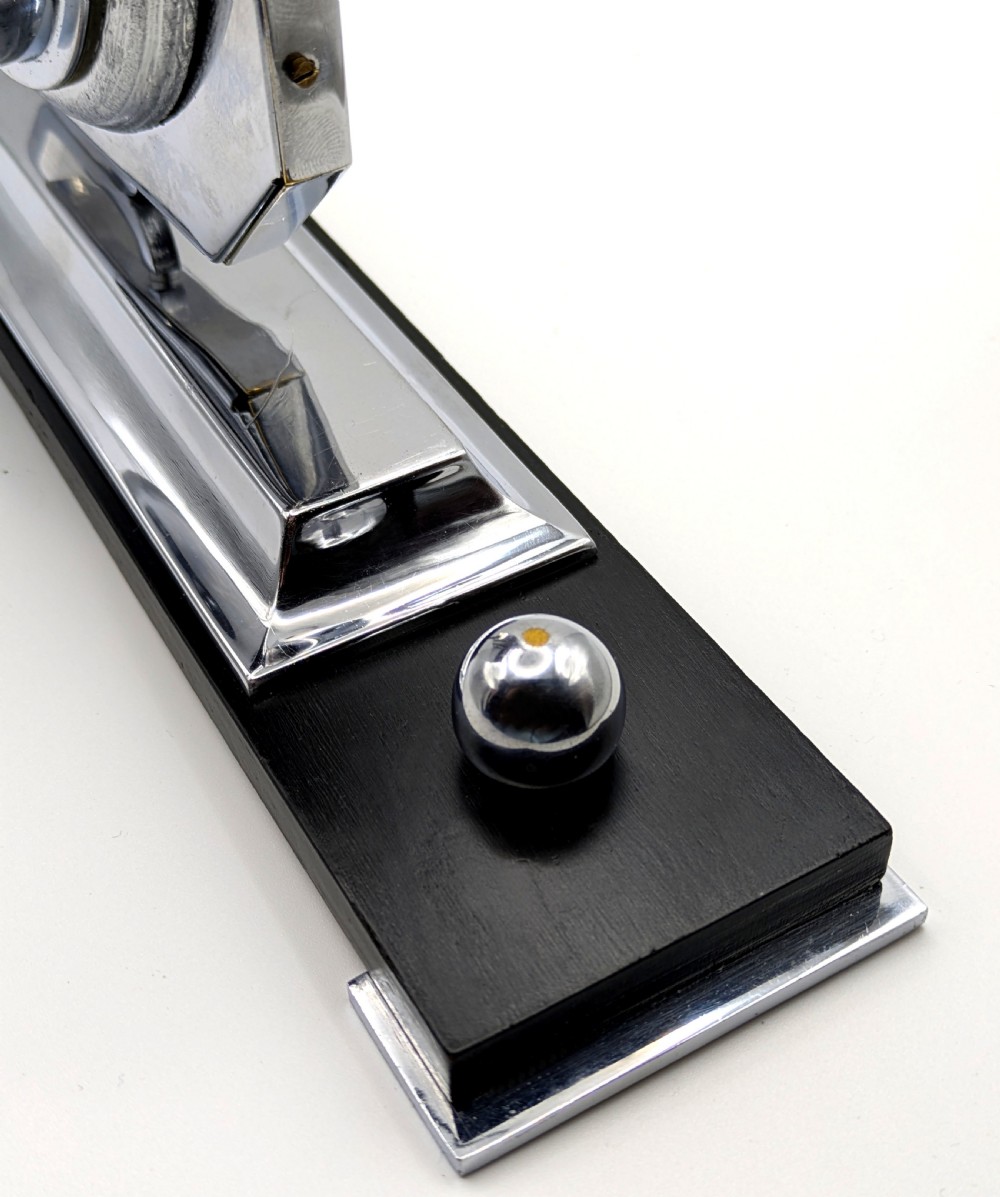 An Art Deco desk clock featuring an octagonal chrome frame mounted on a stepped base with an ebonised plinth and a small chrome sphere detail. View XI