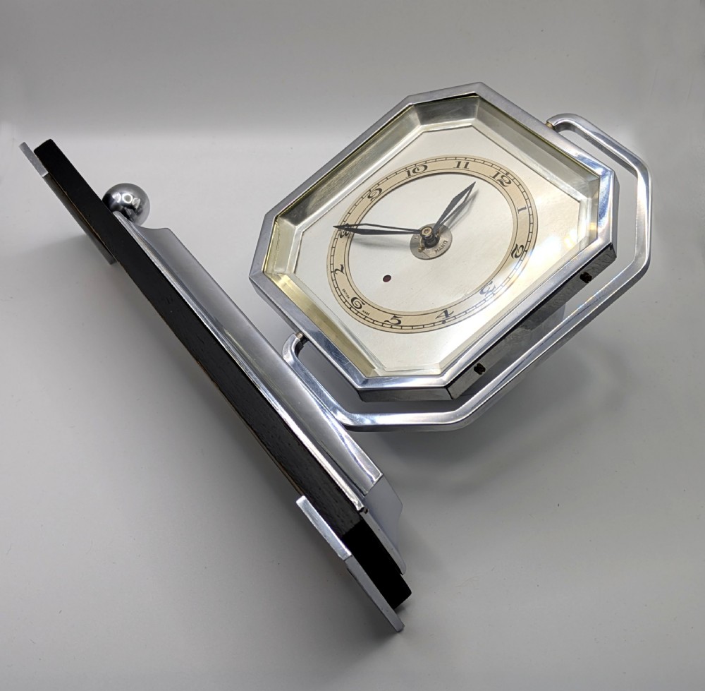 An Art Deco desk clock featuring an octagonal chrome frame mounted on a stepped base with an ebonised plinth and a small chrome sphere detail. View XIII