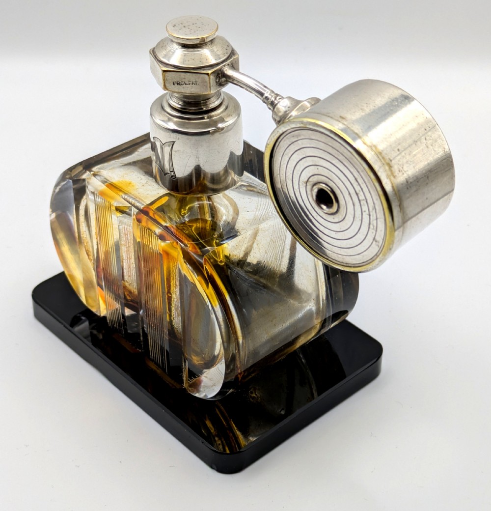 A French Art Deco cut glass perfume atomiser featuring a silver-toned metal spray mechanism mounted on a flat black rectangular base. View III