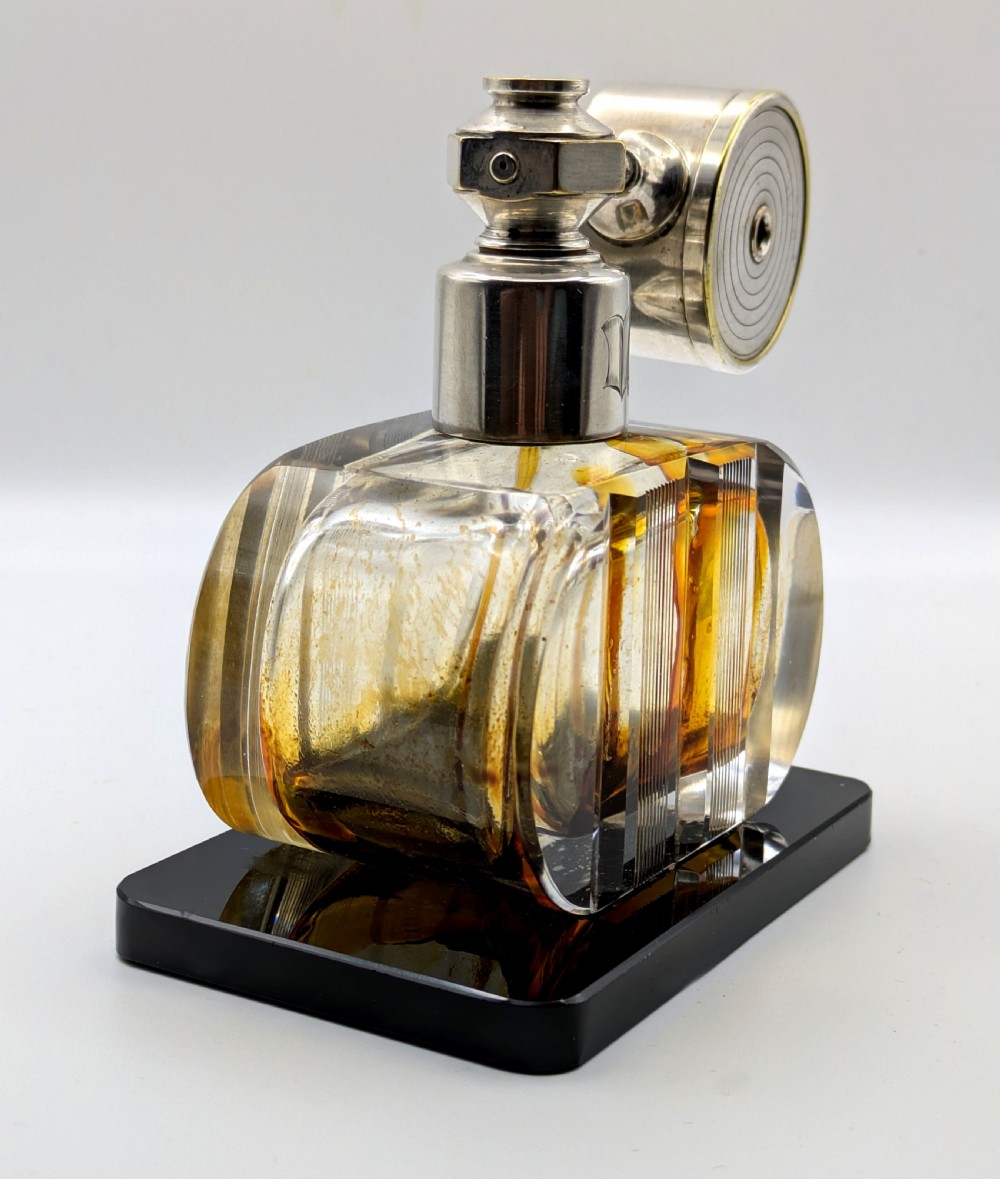 A French Art Deco cut glass perfume atomiser featuring a silver-toned metal spray mechanism mounted on a flat black rectangular base. View V