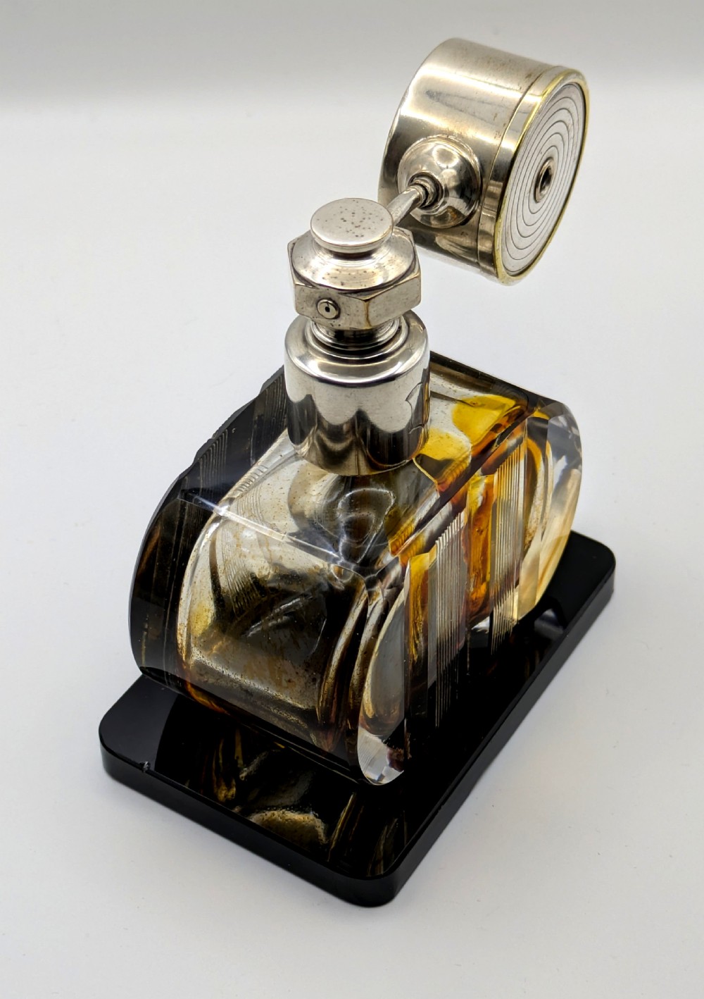 A French Art Deco cut glass perfume atomiser featuring a silver-toned metal spray mechanism mounted on a flat black rectangular base. View VI