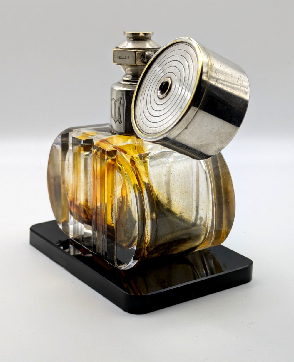 A French Art Deco cut glass perfume atomiser featuring a silver-toned metal spray mechanism mounted on a flat black rectangular base. View XI