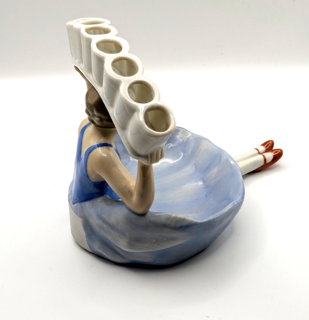 An Art Deco porcelain figurine of a flapper girl wearing a blue dress and holding an arched white and red cigarette holder above her head. View II