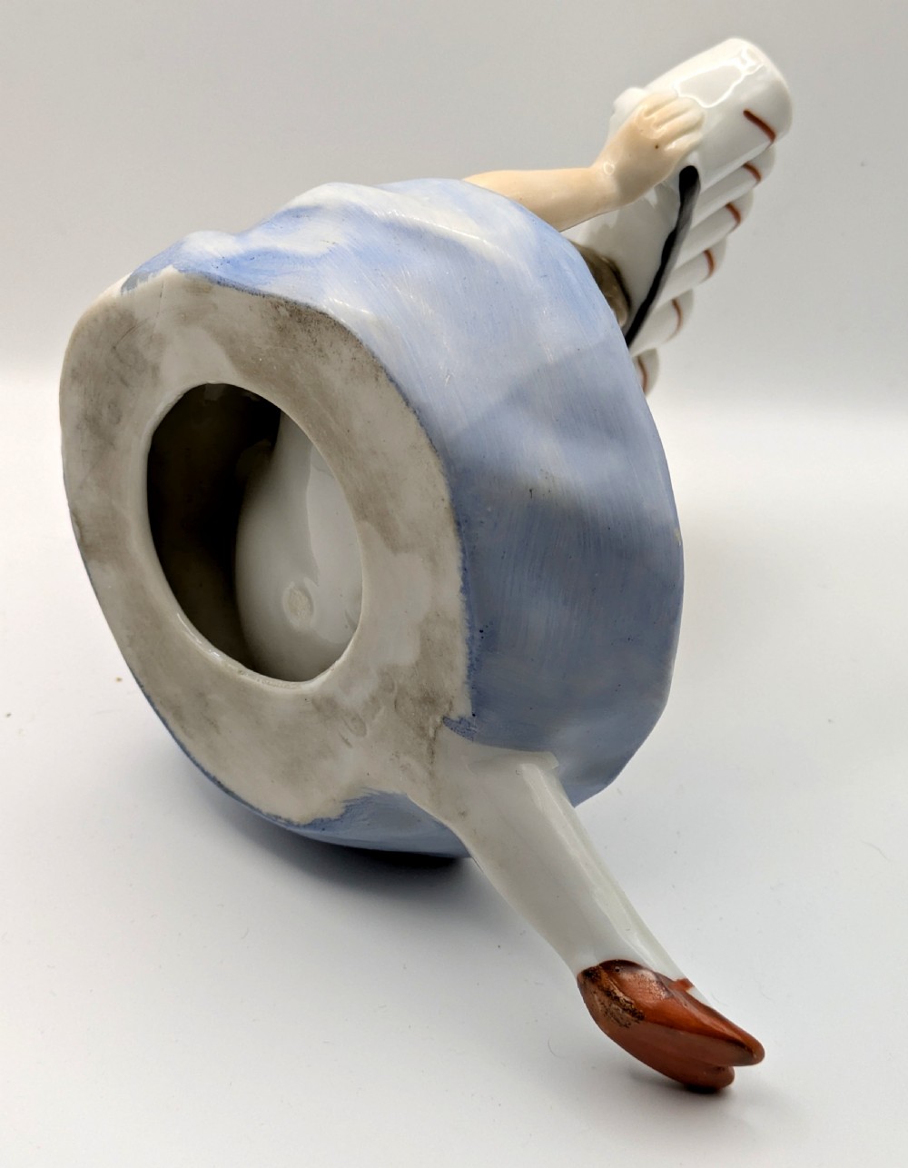An Art Deco porcelain figurine of a flapper girl wearing a blue dress and holding an arched white and red cigarette holder above her head. View V