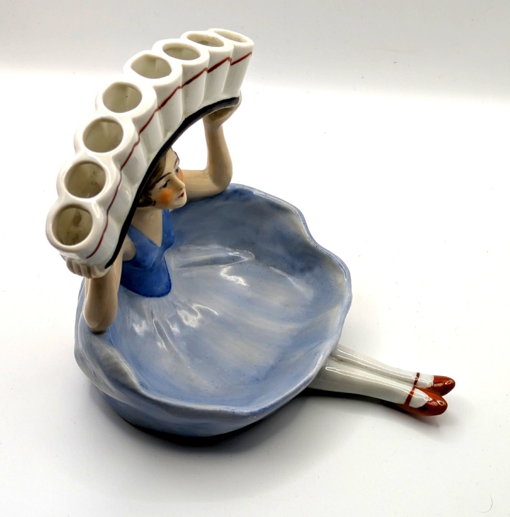 An Art Deco porcelain figurine of a flapper girl wearing a blue dress and holding an arched white and red cigarette holder above her head. View VIII