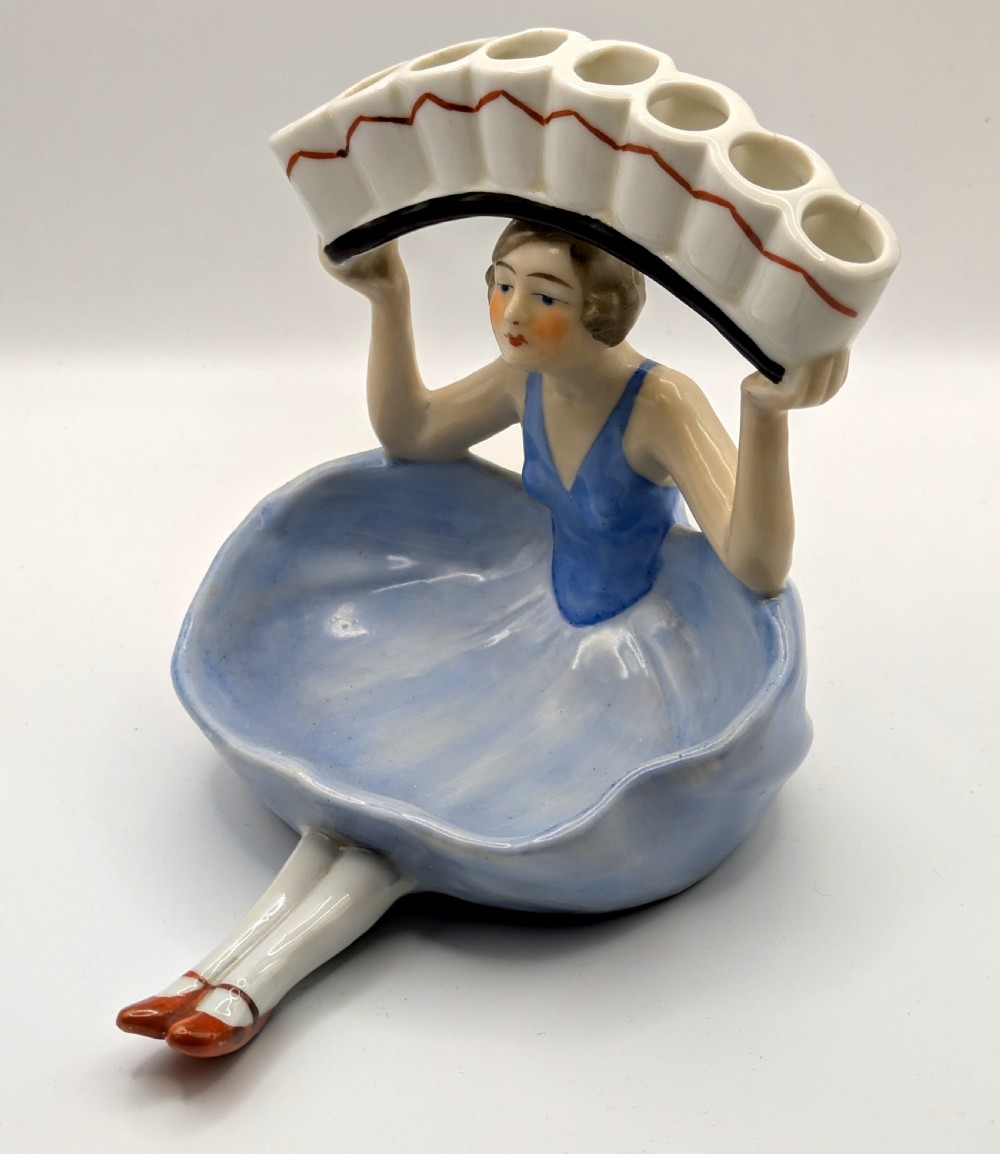An Art Deco porcelain figurine of a flapper girl wearing a blue dress and holding an arched white and red cigarette holder above her head. View IX