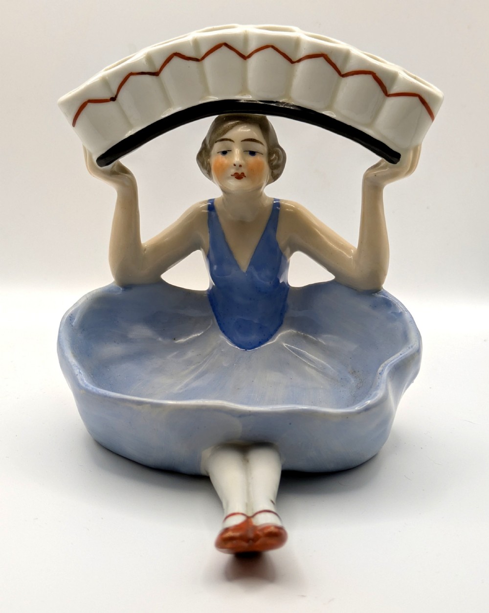 An Art Deco porcelain figurine of a flapper girl wearing a blue dress and holding an arched white and red cigarette holder above her head. View XI