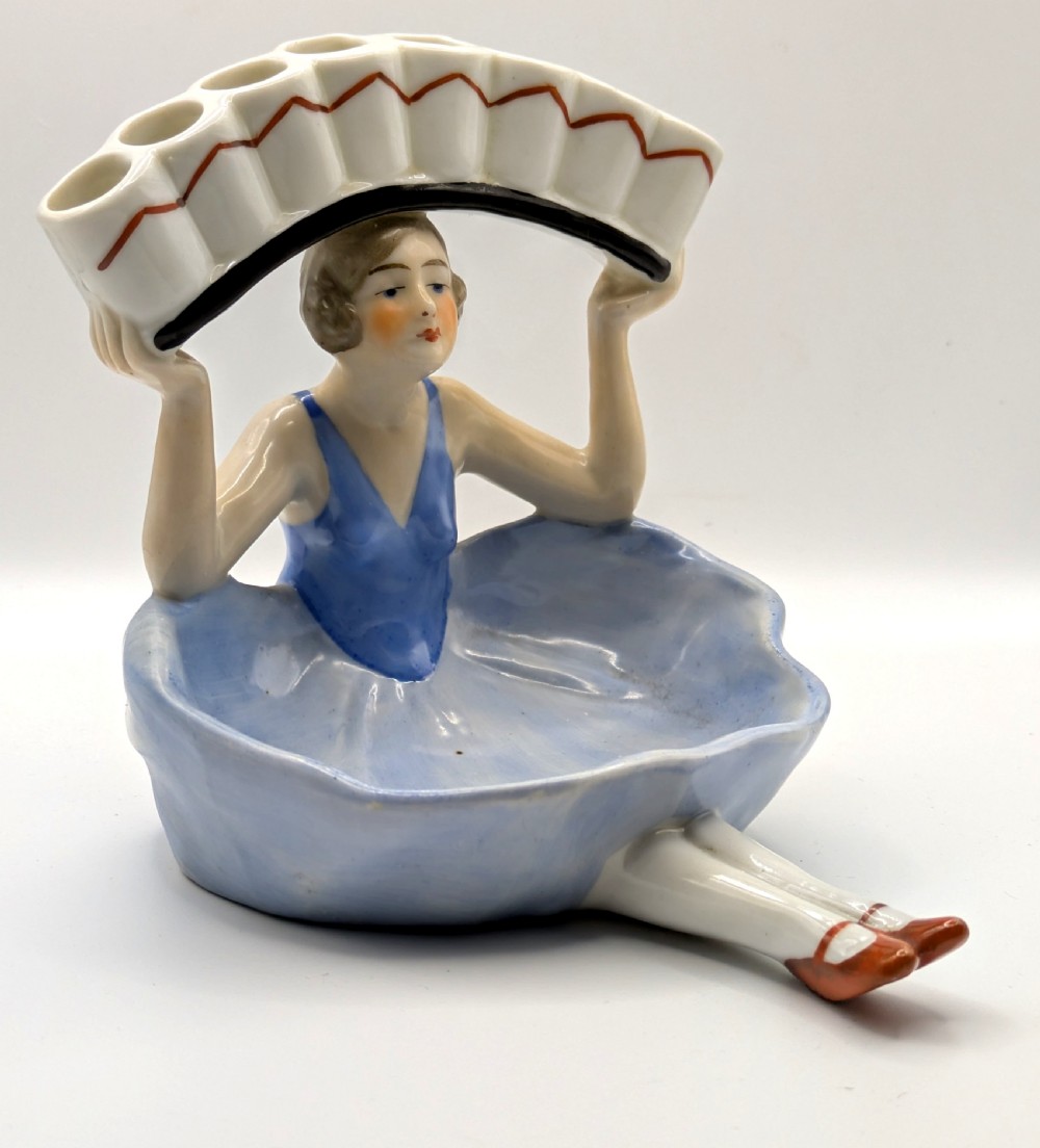 An Art Deco porcelain figurine of a flapper girl wearing a blue dress and holding an arched white and red cigarette holder above her head. View XII