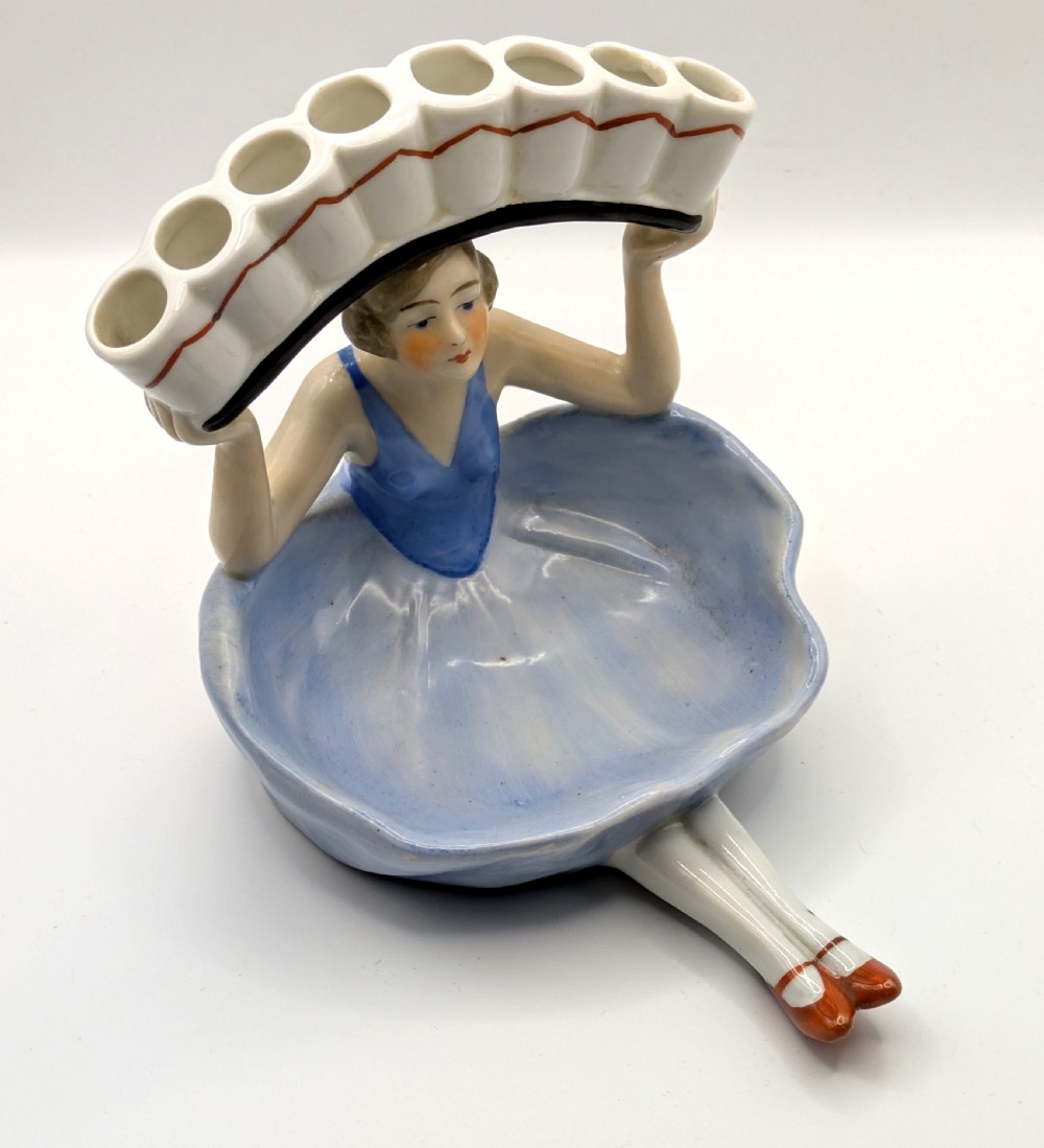 An Art Deco porcelain figurine of a flapper girl wearing a blue dress and holding an arched white and red cigarette holder above her head. View XIII