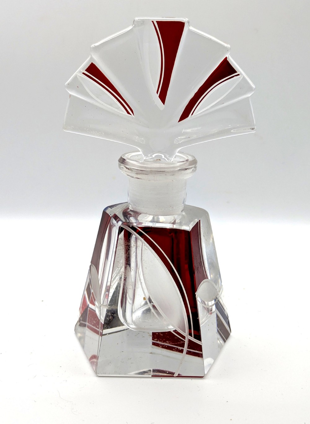 An Art Deco clear glass perfume bottle with red geometric accents and a large fan-shaped stopper. View X
