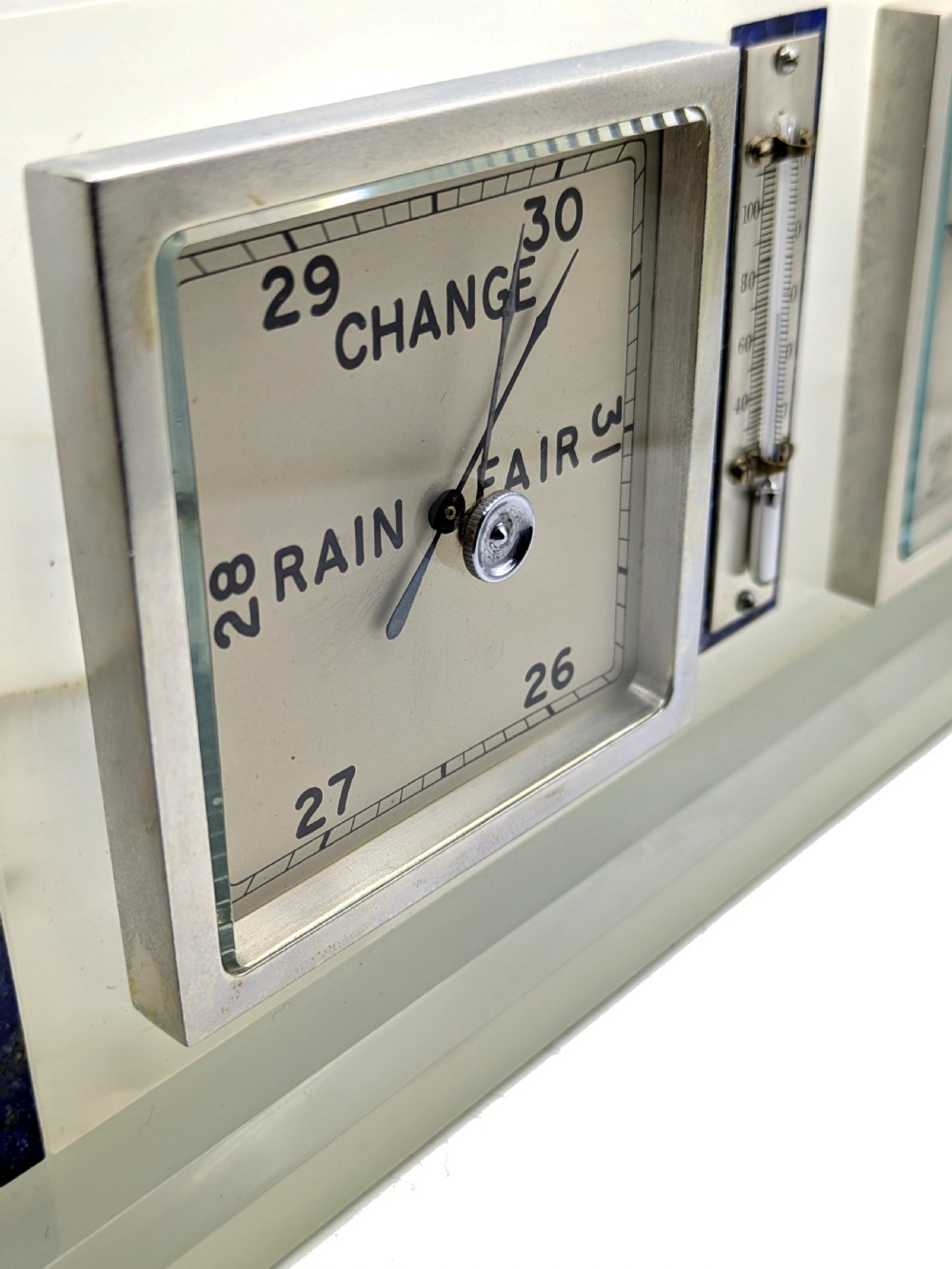 An Art Deco cream onyx desk weather station featuring a square barometer dial, central thermometer, and square clock face flanked by stepped blue lapis lazuli accents. View VII