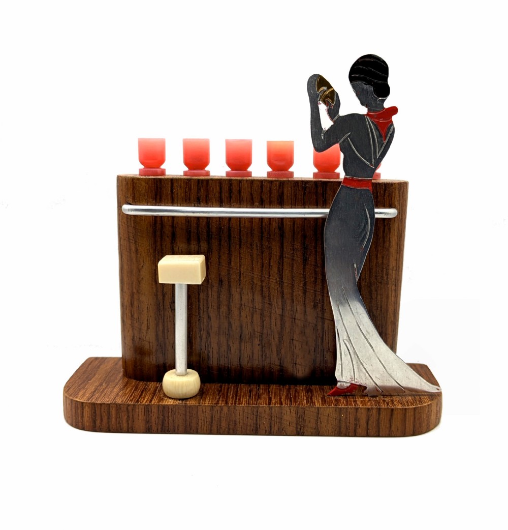 An Art Deco wooden bar stand holding red cocktail picks designed as glasses, with a cut-out silver and red female figure shaking a cocktail shaker. View II