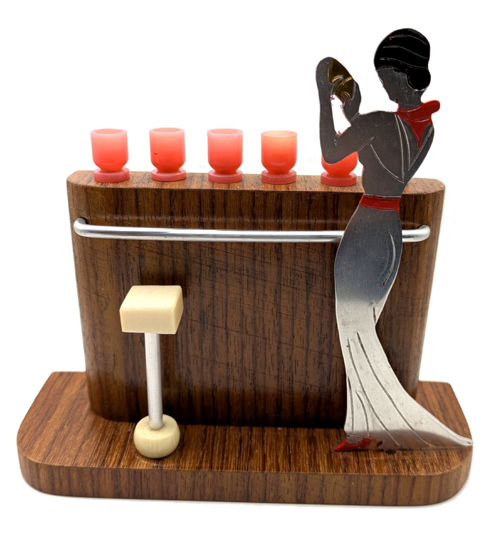 An Art Deco wooden bar stand holding red cocktail picks designed as glasses, with a cut-out silver and red female figure shaking a cocktail shaker. View VIII