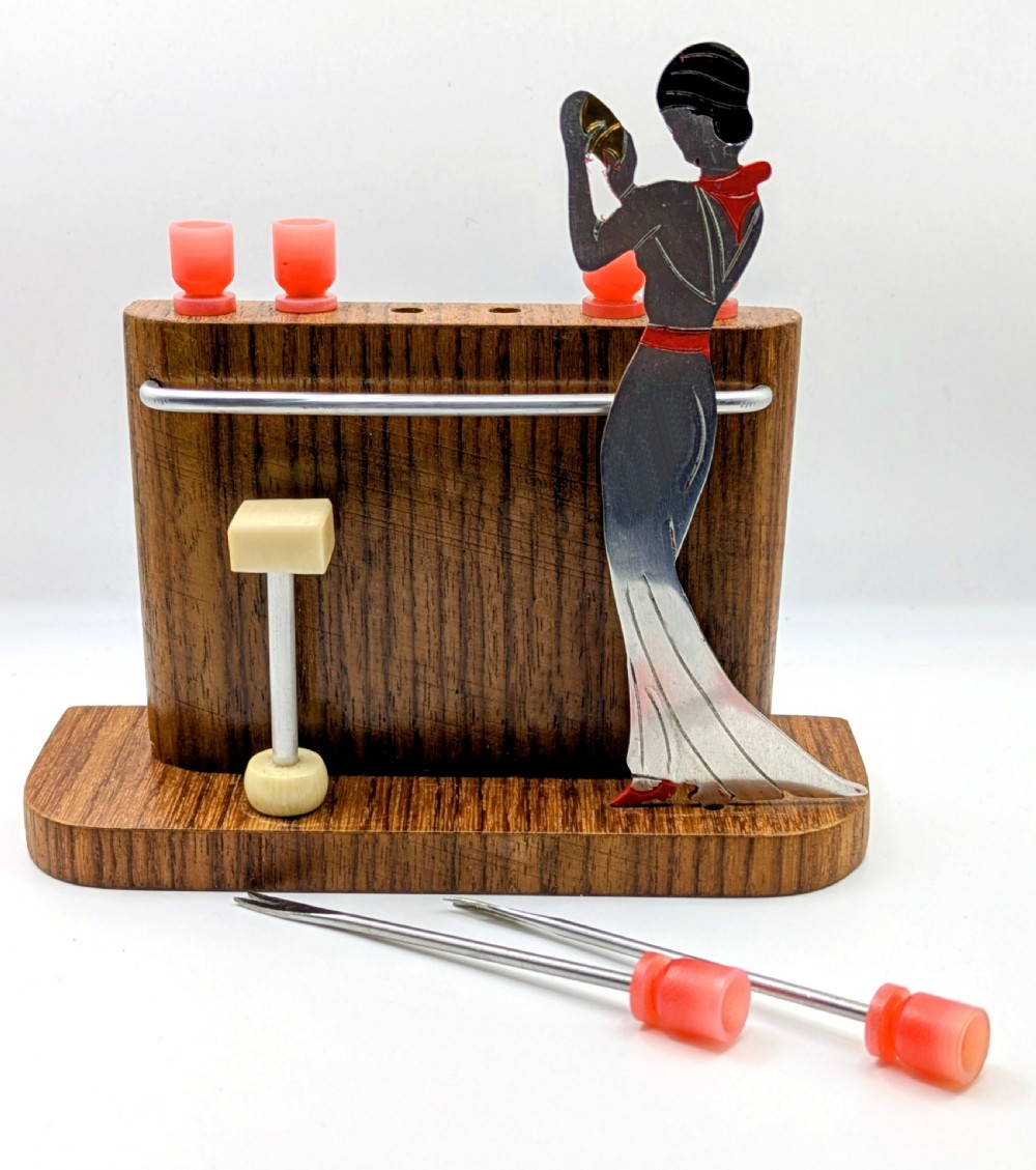 An Art Deco wooden bar stand holding red cocktail picks designed as glasses, with a cut-out silver and red female figure shaking a cocktail shaker. View XI