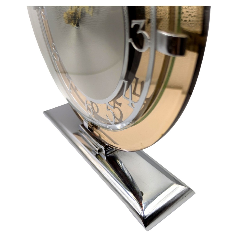 A circular Art Deco mantel clock featuring a peach mirror glass surround, chrome retaining clips, and an etched silver dial set upon a chrome base. View V