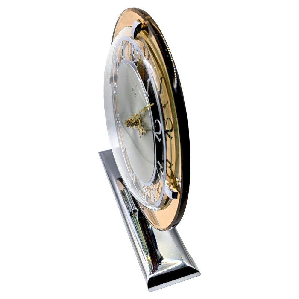 A circular Art Deco mantel clock featuring a peach mirror glass surround, chrome retaining clips, and an etched silver dial set upon a chrome base. View VII