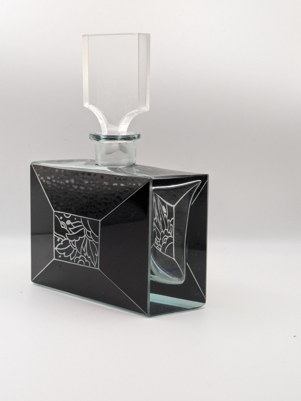 An Art Deco rectangular clear glass perfume bottle featuring black enamelled geometric borders, a central etched floral motif, and a tall rectangular glass stopper. View IV
