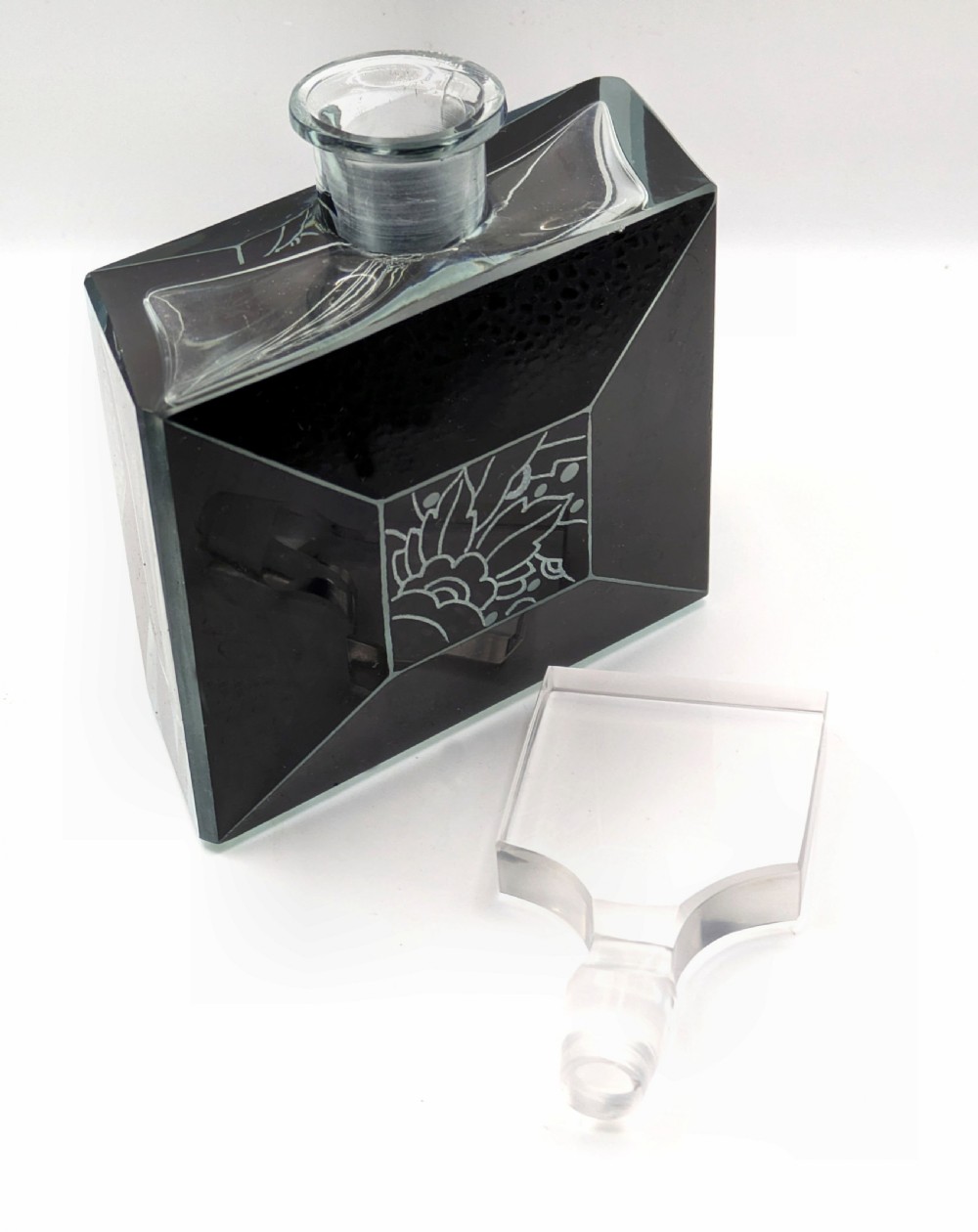 An Art Deco rectangular clear glass perfume bottle featuring black enamelled geometric borders, a central etched floral motif, and a tall rectangular glass stopper. View IX