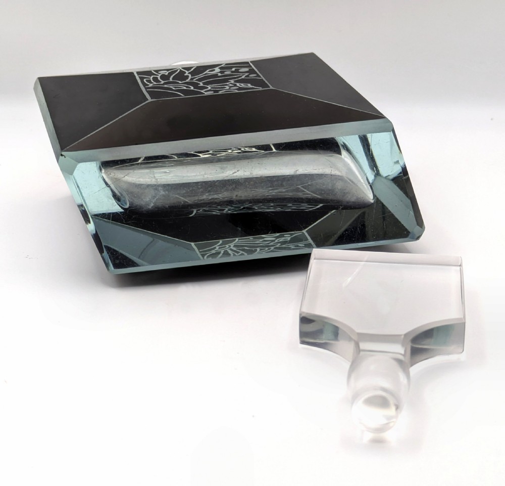 An Art Deco rectangular clear glass perfume bottle featuring black enamelled geometric borders, a central etched floral motif, and a tall rectangular glass stopper. View X