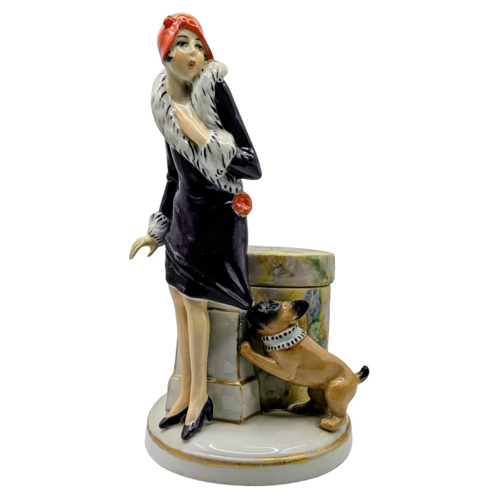 An Art Deco painted porcelain trinket box featuring a flapper lady in a black coat and red cloche hat alongside a small dog.