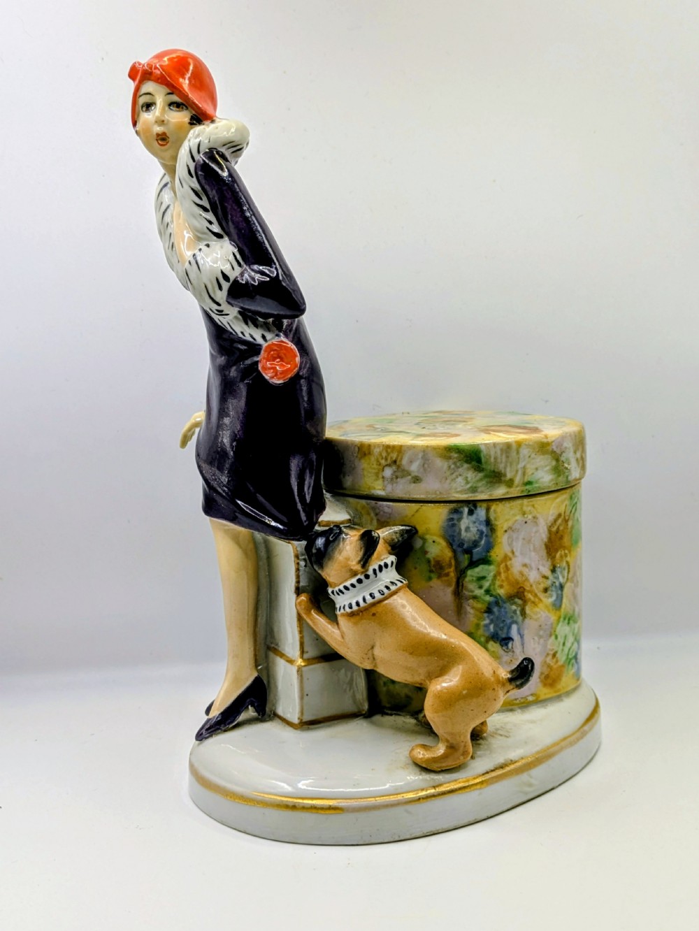An Art Deco painted porcelain trinket box featuring a flapper lady in a black coat and red cloche hat alongside a small dog. View XI