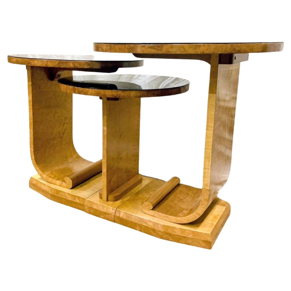 A set of three 1930s Art Deco nesting side tables featuring blonde birds-eye maple curved J-shaped frames and circular black glass insert tops.