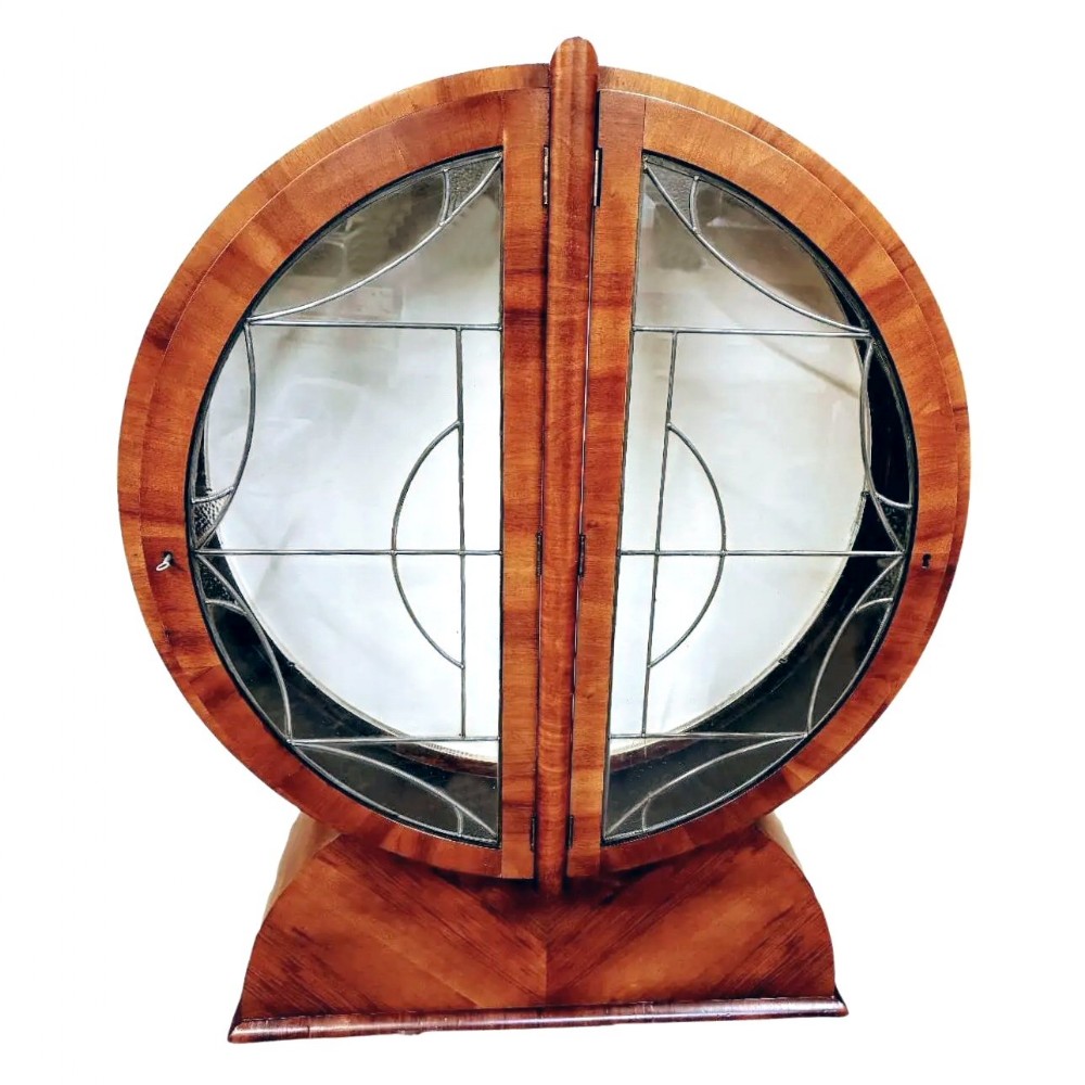 An Art Deco circular walnut display cabinet featuring twin leaded glass doors set on a fitted pedestal base.