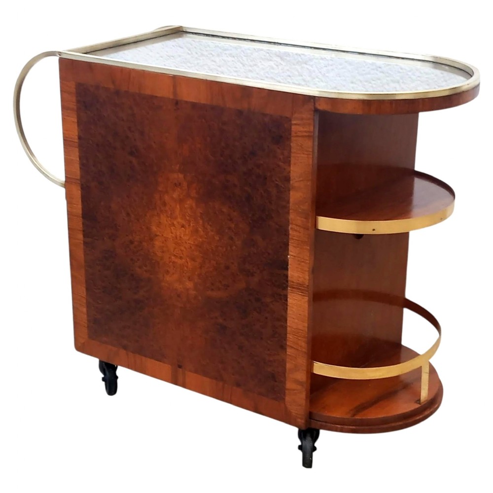 A French Art Deco cocktail bar cart in warm burr amboyna wood featuring open curved shelving, brass galleries, a push handle, and small castors.