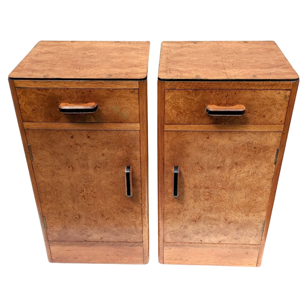 A pair of Art Deco blonde maple bedside cabinets, each featuring a single top drawer and a lower cupboard door with dark wooden handles.