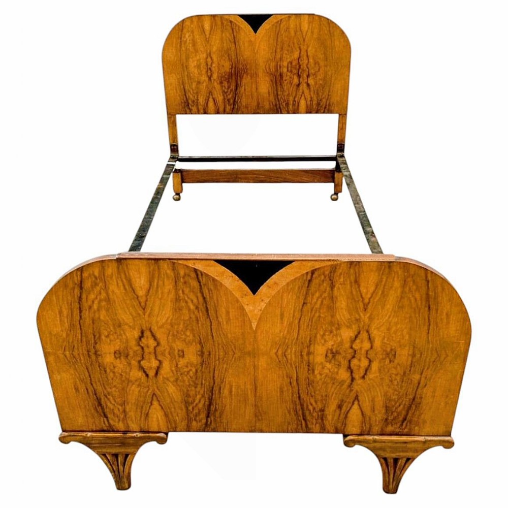 An Art Deco single bed frame featuring book-matched walnut and satinwood veneers, a shaped headboard and footboard with dark inlaid V-motifs, and carved bracket feet.