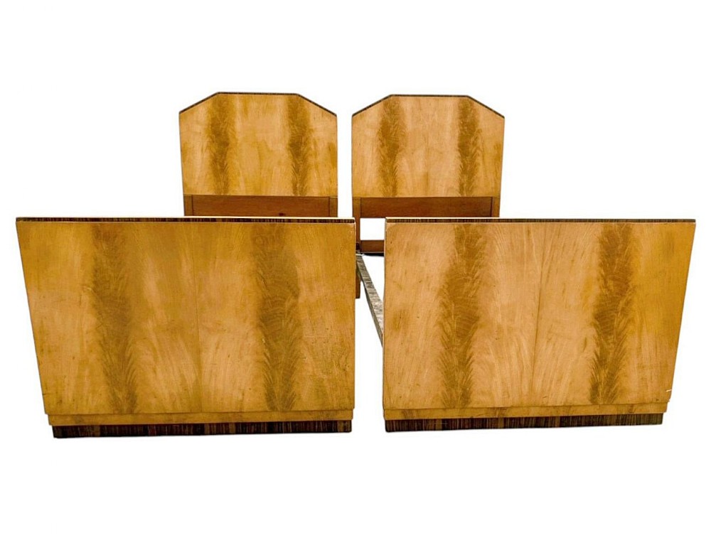 A pair of matching 1930s Art Deco single bed frames featuring bookmatched satinwood and walnut veneers with faceted upper corners.
