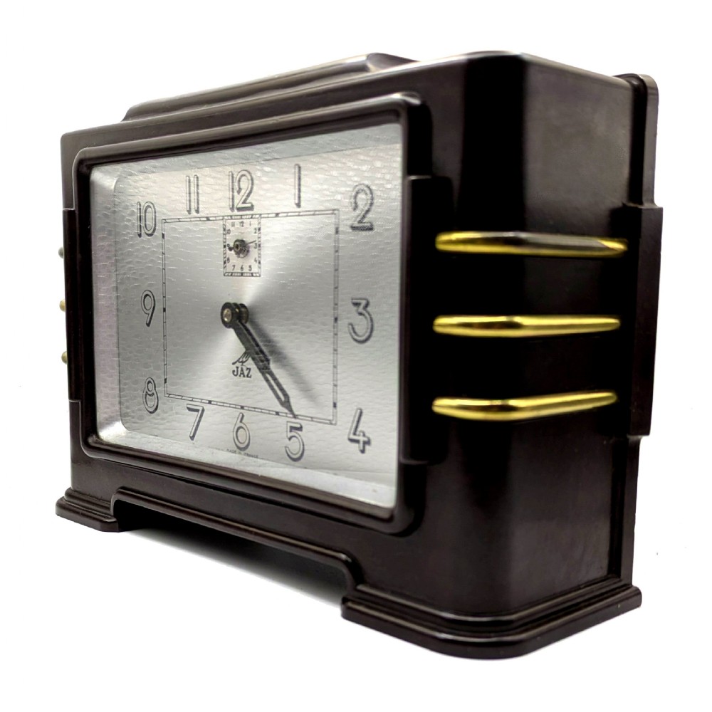 A dark brown rectangular Bakelite mantel clock with gold brass side accents and a silver rectangular dial displaying Art Deco numerals. View III