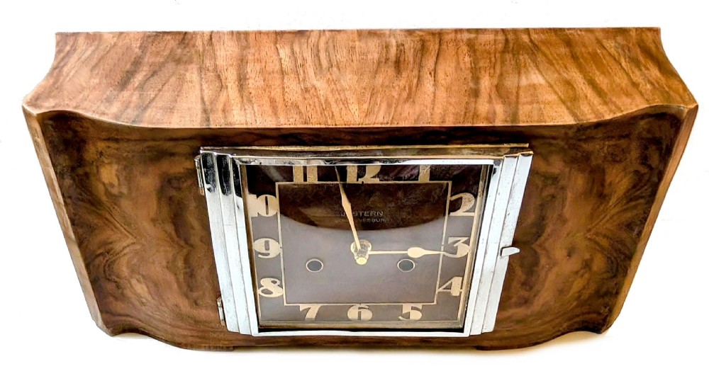 An Art Deco horizontal mantel clock crafted from figured walnut veneer featuring a square glass dial set within a polished chrome frame. View XI
