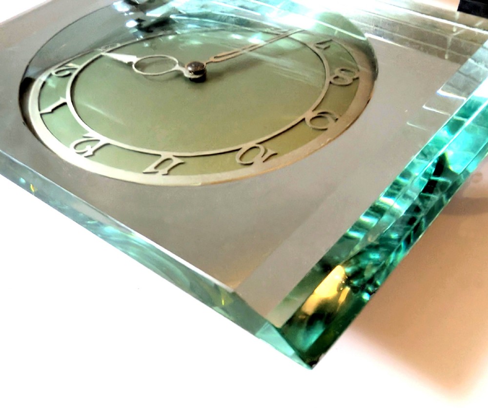 An Art Deco mantel clock featuring a thick rectangular glass body held by chrome scroll mounts on a flat metal base. View III