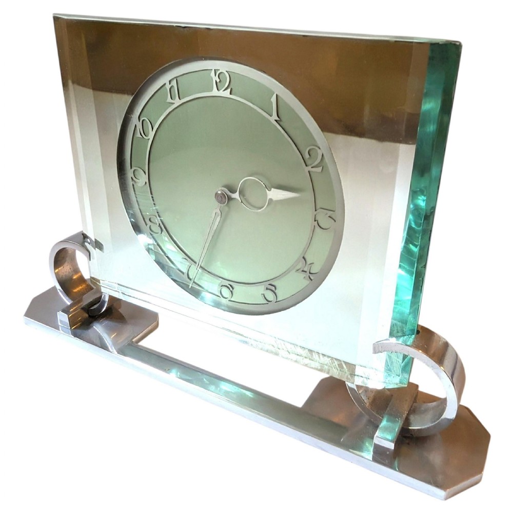 An Art Deco mantel clock featuring a thick rectangular glass body held by chrome scroll mounts on a flat metal base. View VII