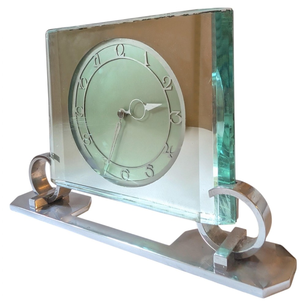 An Art Deco mantel clock featuring a thick rectangular glass body held by chrome scroll mounts on a flat metal base. View X